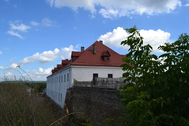 Білий корпус князівського палацу з черепичним дахом над кам'яним муром Дубенського замку