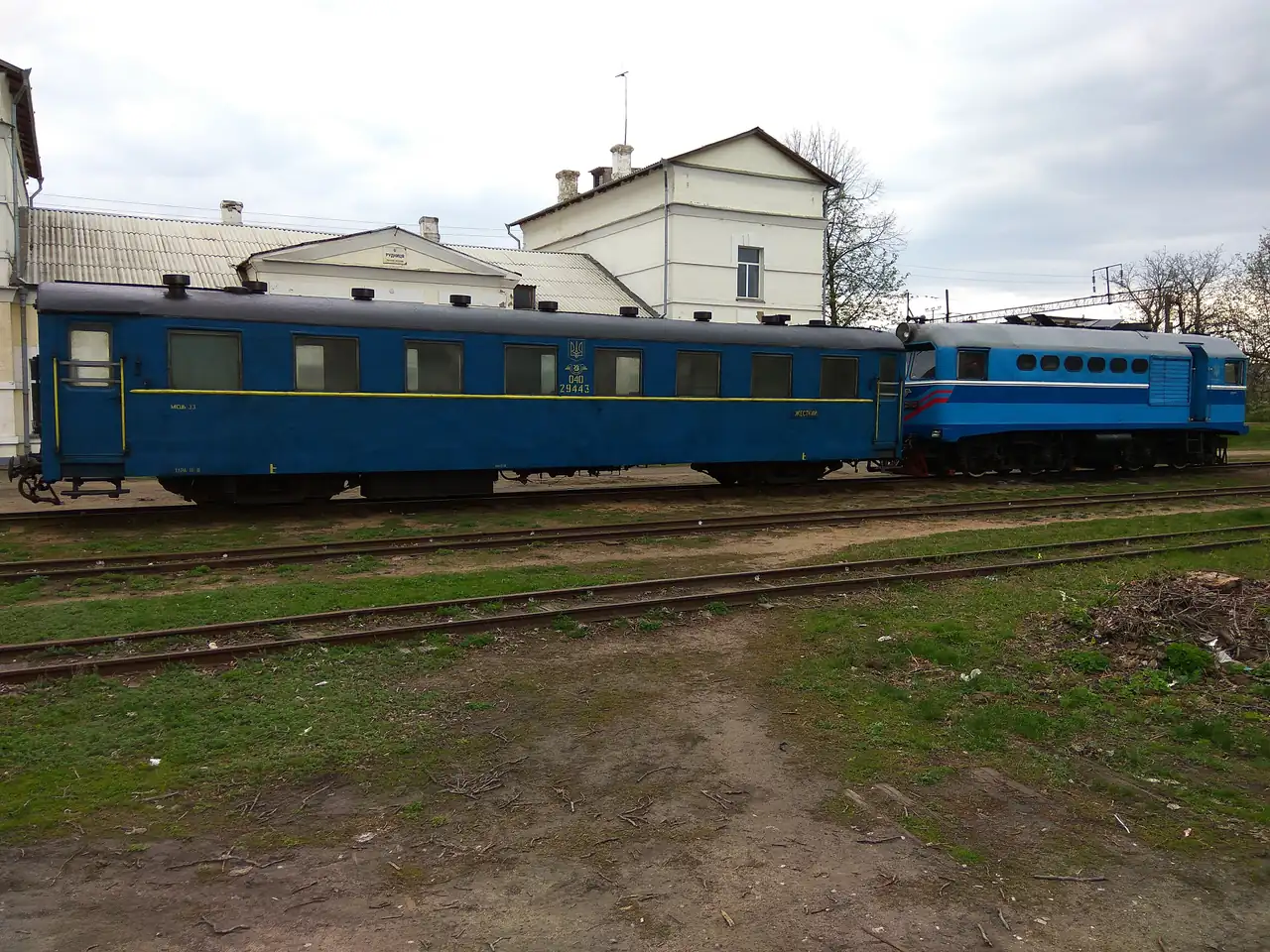 Синій вузькоколійний пасажирський вагон із тризубом і тепловоз на станції Рудниця