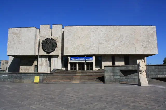 Будівля Музею історії міста Кам’янського: облицьований світлим каменем модерністський корпус із широкими сходами та круглим рельєфом на глухій стіні