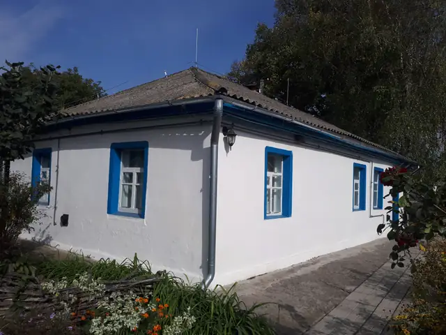 Побілена сільська хата музею-садиби Катерини Білокур із блакитними лиштвами вікон і чотирисхилим черепичним дахом
