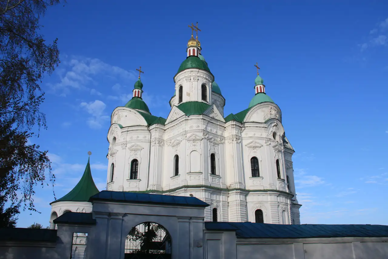 Собор Різдва Богородиці в Козельці: білий об’єм із насиченим ліпленням і п’ятьма зеленими банями, попереду мурована огорожа з брамою