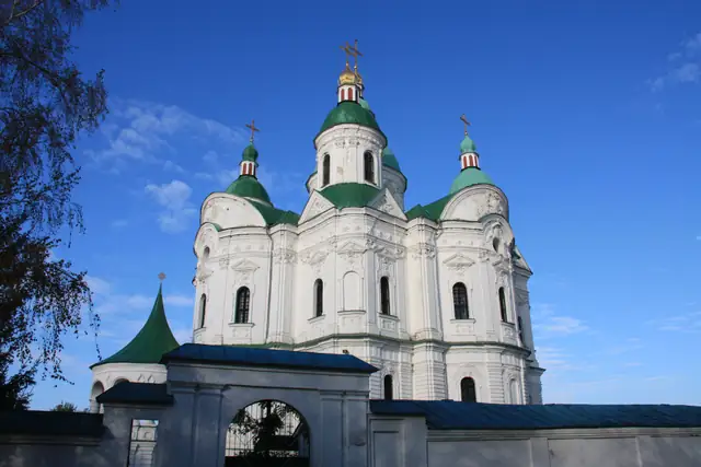 Собор Різдва Богородиці в Козельці: білий об’єм із насиченим ліпленням і п’ятьма зеленими банями, попереду мурована огорожа з брамою