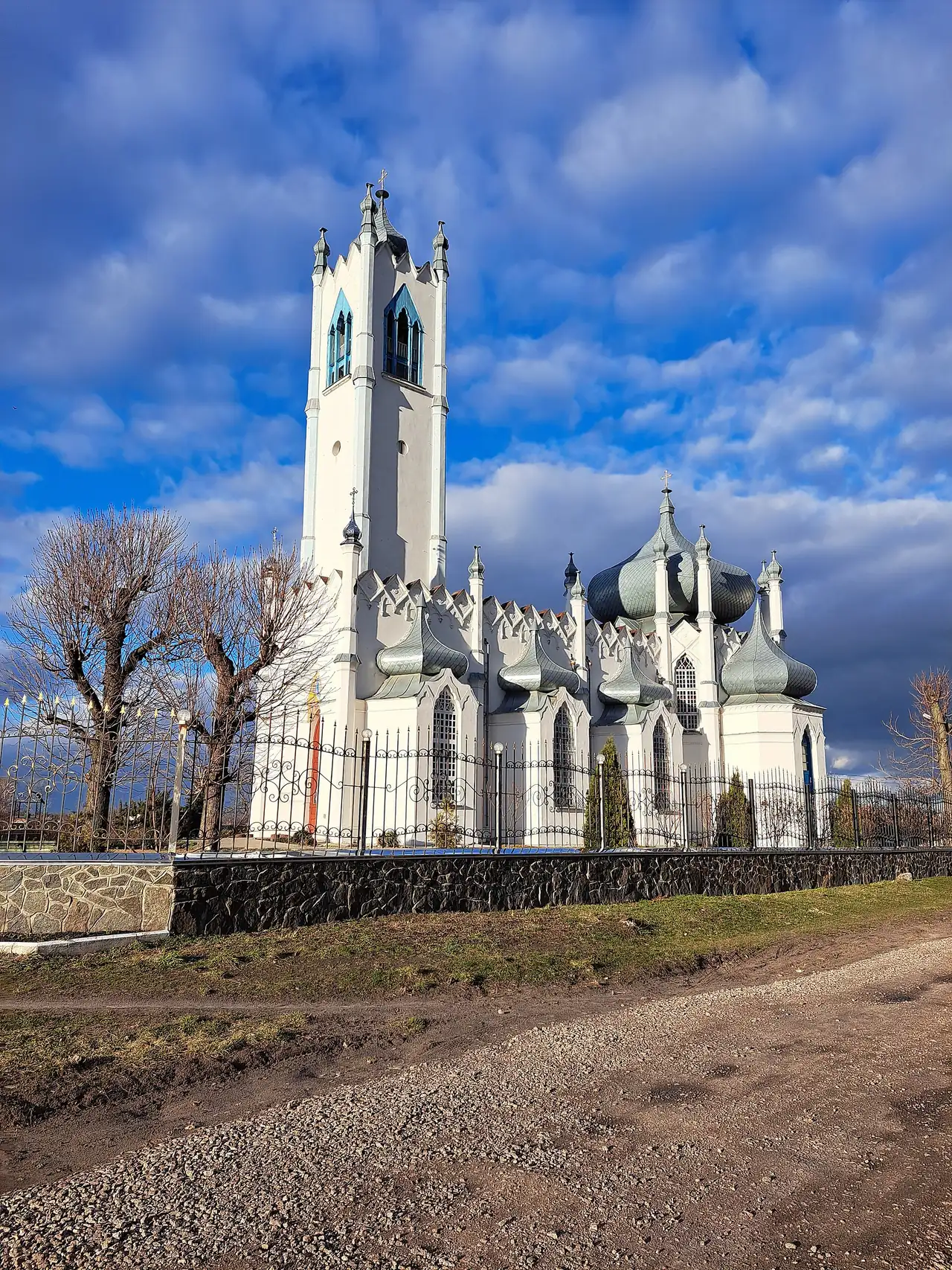 Біла Спасо-Преображенська церква в Мошнах: висока вежа-дзвіниця з пінаклями та ряд зелених цибулястих бань