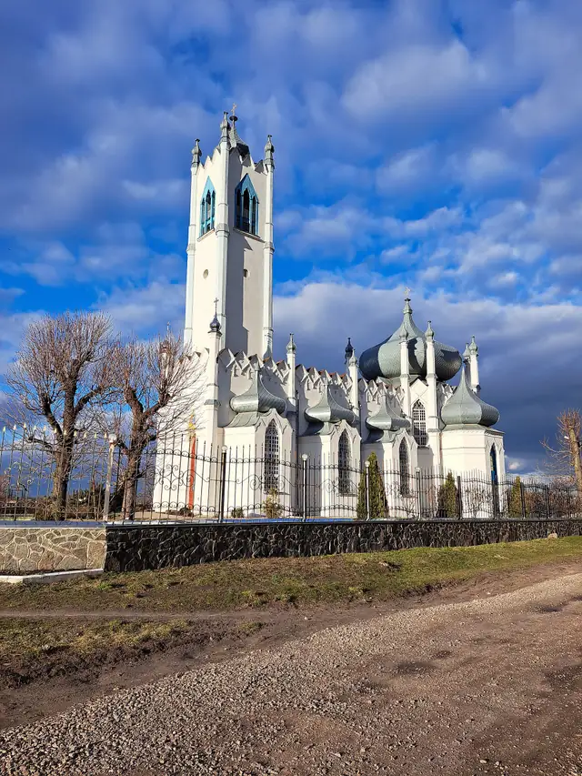 Біла Спасо-Преображенська церква в Мошнах: висока вежа-дзвіниця з пінаклями та ряд зелених цибулястих бань