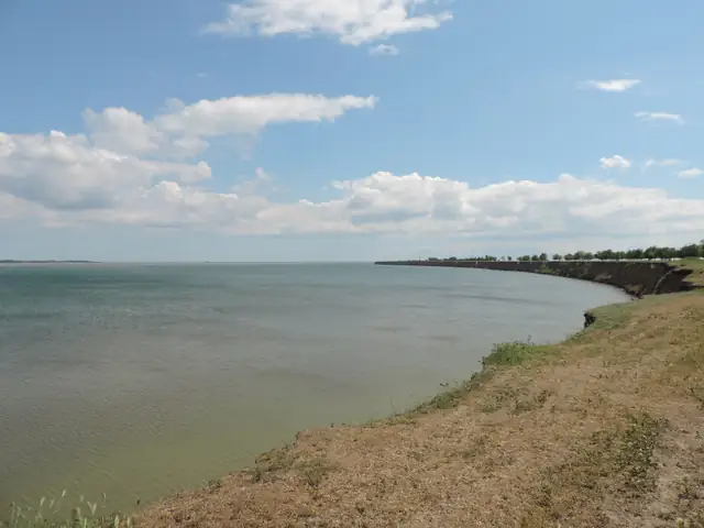 Берег лиману Бурнас: широка водна гладь, вигнута лінія низького глинистого обриву й випалена степова трава